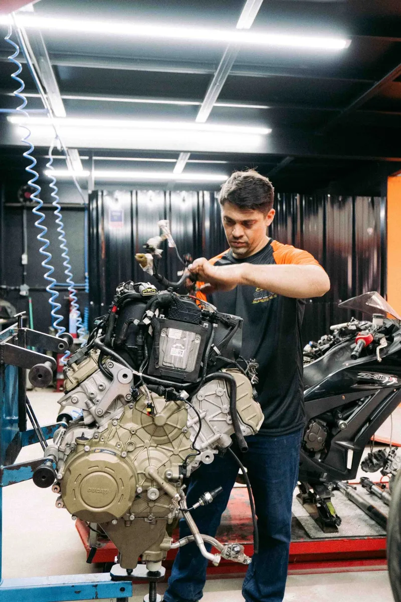 Edilson trabalhando em um motor retirado da moto, apoiado no cavalete